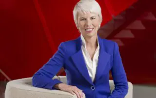 A professional corporate portrait of Gail Kelly, former CEO of Westpac, seated in a modern setting with a striking red background, taken for the Westpac Annual Report. Corporate photography by Sydney photographer Gavin Jowitt.